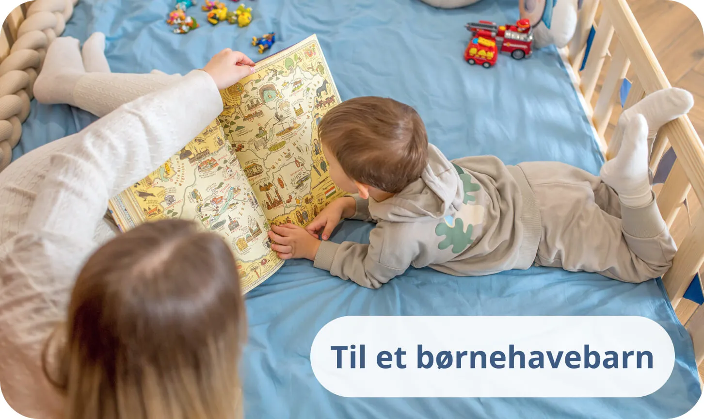 Lille dreng med sin mor læser en farverig bog på blåt sengetøj i en fyrretræsseng.